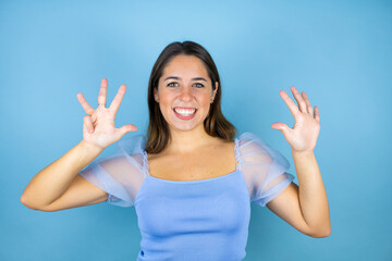 Young beautiful woman over isolated blue background showing and pointing up with fingers number...
