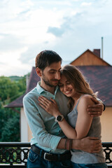 Fototapeta premium Man embracing wife at balcony. Relaxed couple enjoy day and good news. Happy young family