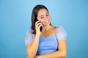 Young beautiful woman over isolated blue background smiling while talking on the phone