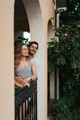 Man embracing wife at balcony. Relaxed couple enjoy day and good news. Happy young family