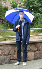 Young man in medical mask and gloves under rain in park during coronavirus pandemic (covid-19)