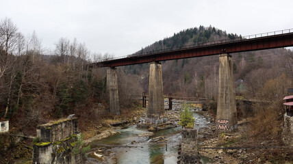 Fototapeta na wymiar View of the railway bridge over the Prut river. A small town or village of Yaremche among the Carpathians on an autumn afternoon.