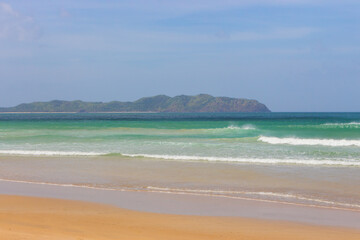 Empty tropical beach on sunny day. Duli beach in Palawan, Philippines. Surf beach. Wide beach with island on background. Travel in Asia. Tropical landscape. Azure water in idyllic lagoon. 