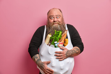 Obese bearded European man has excess weight because of unhealthy harmful nutrition, carries...