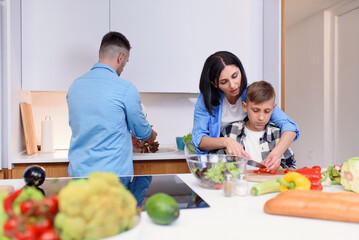 Cooking a healthy family dinner together in the kitchen together. Mom teaches her son to cut vegetables for salad.