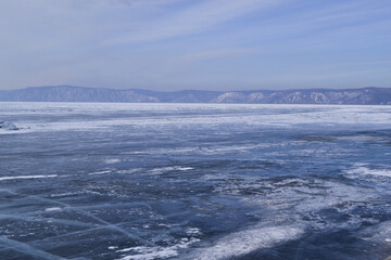 Naklejka na ściany i meble large iridescent crystals white blue ice with cracks glow in the light of the sun, lake baikal in winter, mountains on the horizon