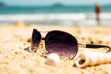 Sunglasses lying on a tropical sandy beach with seashells and stones. Sunglasses on the beach. Nice sea view. Vacation, travel concept