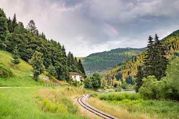 Fototapeta na wymiar Railway in a scenic valley in the Alps. Part of a rainbow over the mountains.