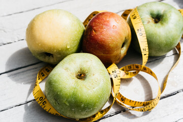 Delicious and healthy food is on the kitchen table. Four apples-yellow, green and red on a white wooden background and a yellow flexible centimeter ribbon.
