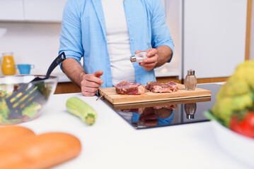 Man pours salt on raw meat steaks with at cozy modern kitchen. Barbecue concept and tasty food.