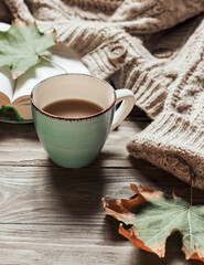 Autumn morning coffee. A cup of coffee on a wooden table and a warm sweater on a background of autumn leaves. Still life concept. Copy space.