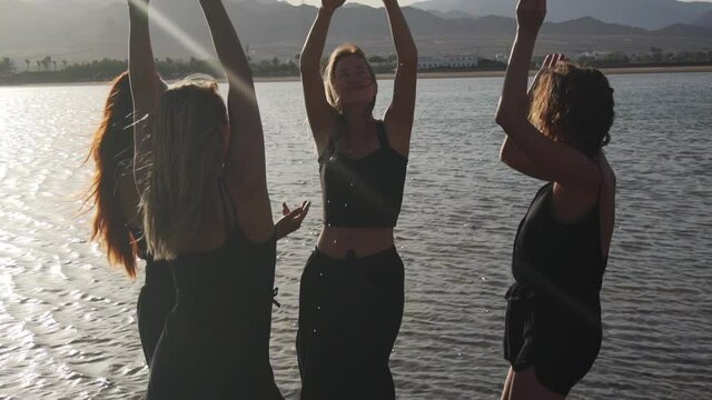 group of attractive females dancing ecstatic in sea at sunset slow motion