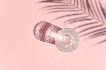 A glass with water in sun rays seen top view. Palm leaf shadow.