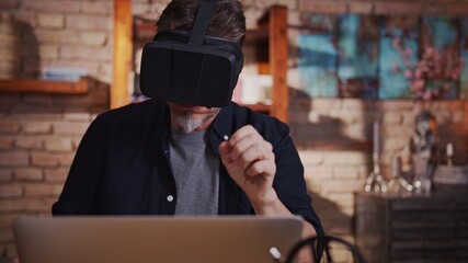 Casual man man working with virtual reality googles at home sitting at desk with laptop computer in...