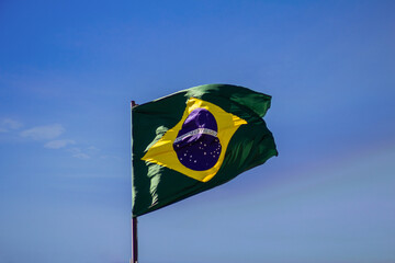 Bandeira do Brasil hasteada e tremulando ao vendo com céu ao fundo.