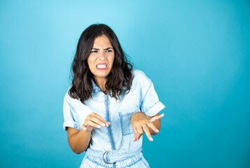 Young beautiful woman wearing a denim jumpsuit over isolated blue background disgusted expression,...