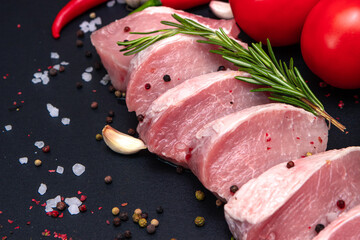 Raw juicy meat steaks ready for roasting on a black chalk board background. fillet with cherry tomatoes, hot pepper and herbs.