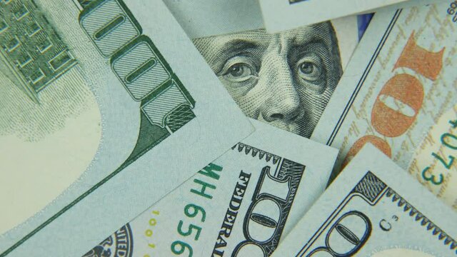 One-hundred-dollar bills rotate. Franklin's eyes peek out of a stack of money.