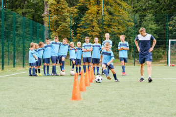 Kids player run and kick soccer balls between soccer chips in soccer training