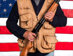 Man holding shotgun wearing shooting hunting vest in front of American flag, weapon, gun laws,...