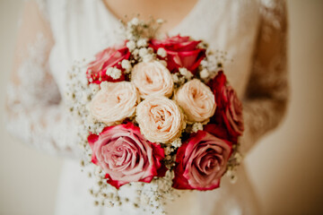 female holding bridal bouquet. Bouquet made of red and white roses in the circular shape. Women in the white decorated wedding dress.  A closeup whit blurred background in simetrical composition. 