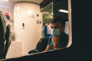 Tired and sad male passenger sits in face shield and looks through the window. View through the window. Topic passenger public transport during coronavirus pandemic. New rules of life covid 19