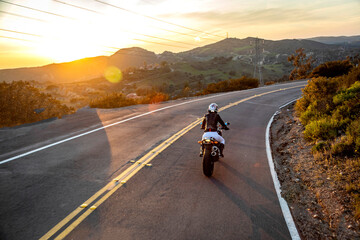 Motorcycle rider at sunset with white pants shot from behind driving up Modjeska Grade Road,...
