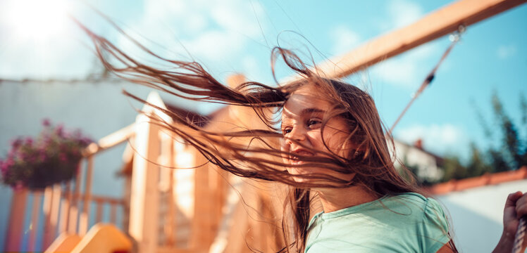 Portrait of a happy little girl sitting on a swing with long hair flying