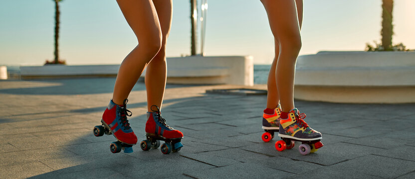 Cropped image of two women in swimsuits rollerblading near the beach in sunny weather.