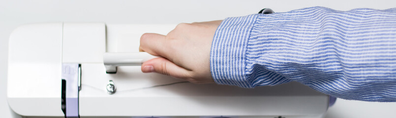 The girl holds the handle of a sewing machine. White sewing machine.