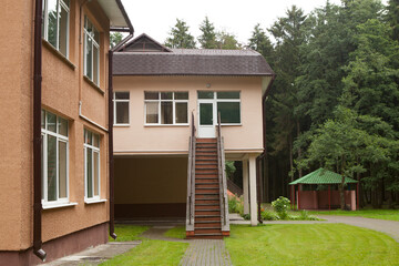 A staircase is an entrance to the second floor of a two-story administrative building of a children's center or hospital, clinic. Green trees and bushes in summer.