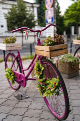 Fototapeta na wymiar Retro purple bicycle on roadside decorated with vintage wood box full of flowers on city building background