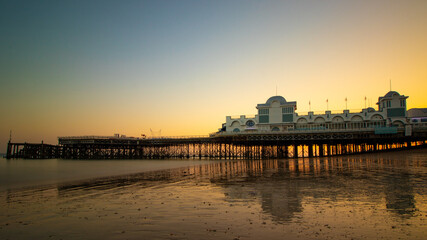 An english pier reflecting on wet sand at sunset, south parade pier, Southsea