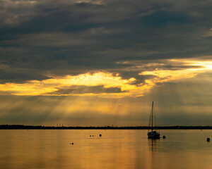 Naklejka na ściany i meble Light rays through the clouds at sunset shining down on a single yacht or sailing boat 