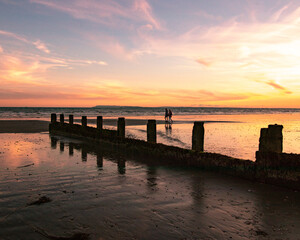 Fototapeta premium A couple walking along a sandy beach at sunset 