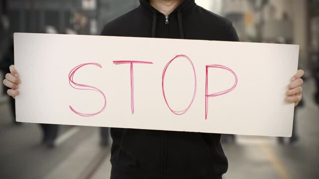 Activist wearing black holds a placard with STOP text