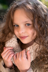 Portrait of little cute smiling girl  with long curly hair in stylish retro coat walking in the garden or park.