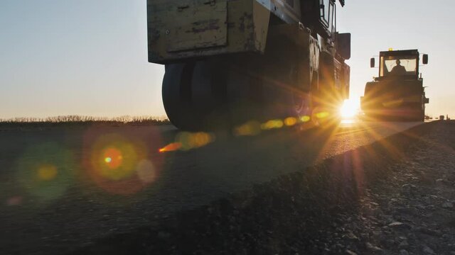 Two road rollers line the asphalt at sunset. Road surface repair. Construction of a new road. Road construction machines. A layer of freshly laid asphalt.