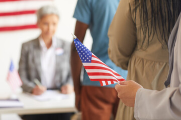 Close up of female hand holding American flag against background of polling station on election day, copy space