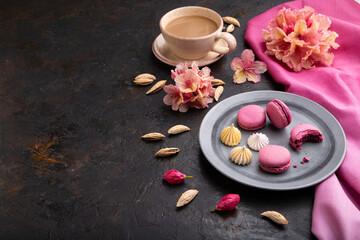 Obraz na płótnie Canvas Purple macarons or macaroons cakes with cup of coffee on a black concrete background. Side view, copy space.