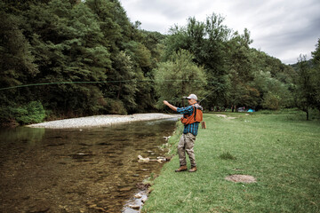 Obraz premium Senior man is fishing alone on fast mountain river. Active people and sport fly fishing concept.