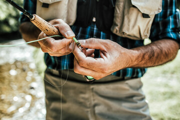 Close up shot of senior fisherman's hands tying a fly for fishing. Fly fishing concept.