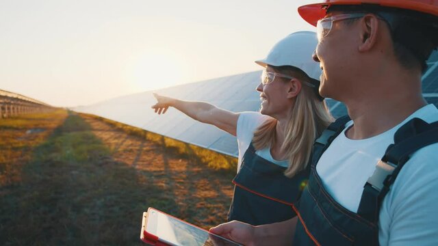 Cheerful caucasian woman technician with chief asian engineer discussing solar panels installation construction of ecological power plant smiling together.