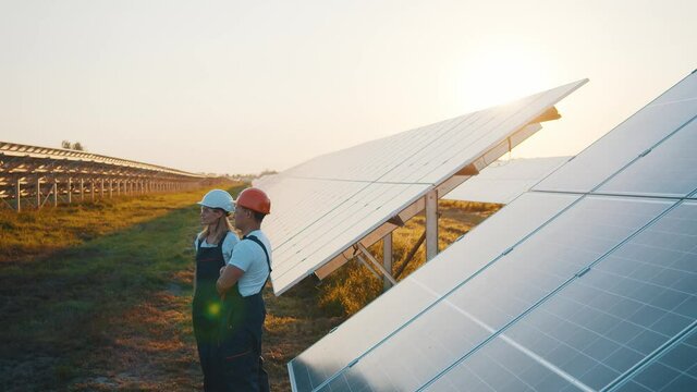 Green Future. Clean Energy. Couple Of Professional Workers Standing And Controlling Work Of Photovoltaic Renewable Energy Solar Panel Batteries At Farmland.