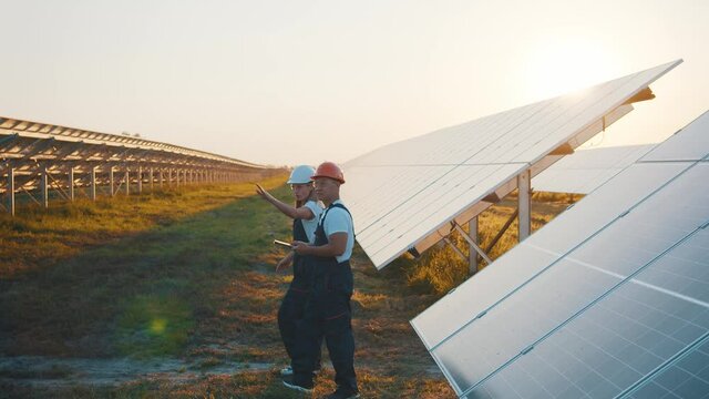 Asian and caucasian workers discovering ecological farmland with rows of solar batteries using tablet computer for repairment. Ecological field. Solar energy.
