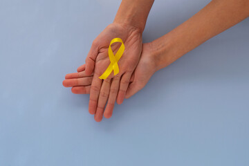 Hands holding yellow gold ribbon over blue sky, sarcoma awareness, bone cancer, childhood cancer awareness, September yellow, world suicide prevention day concept