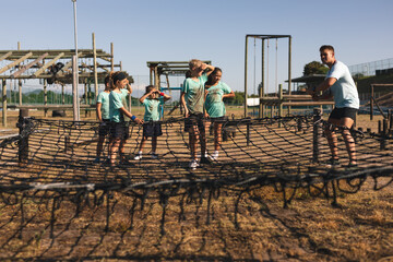 Male fitness coach and kids standing on rope net at a boot camp