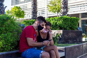 Pareja joven con mascarilla respetando el distanciamiento social en un espacio publico. 