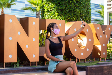 Mujer joven con mascarilla tomandose fotos selfie en un sitio publico 