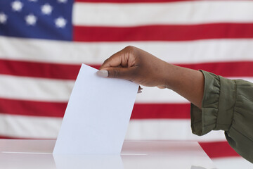 Side view close up of unrecognizable African-American woman putting vote in ballot box against...